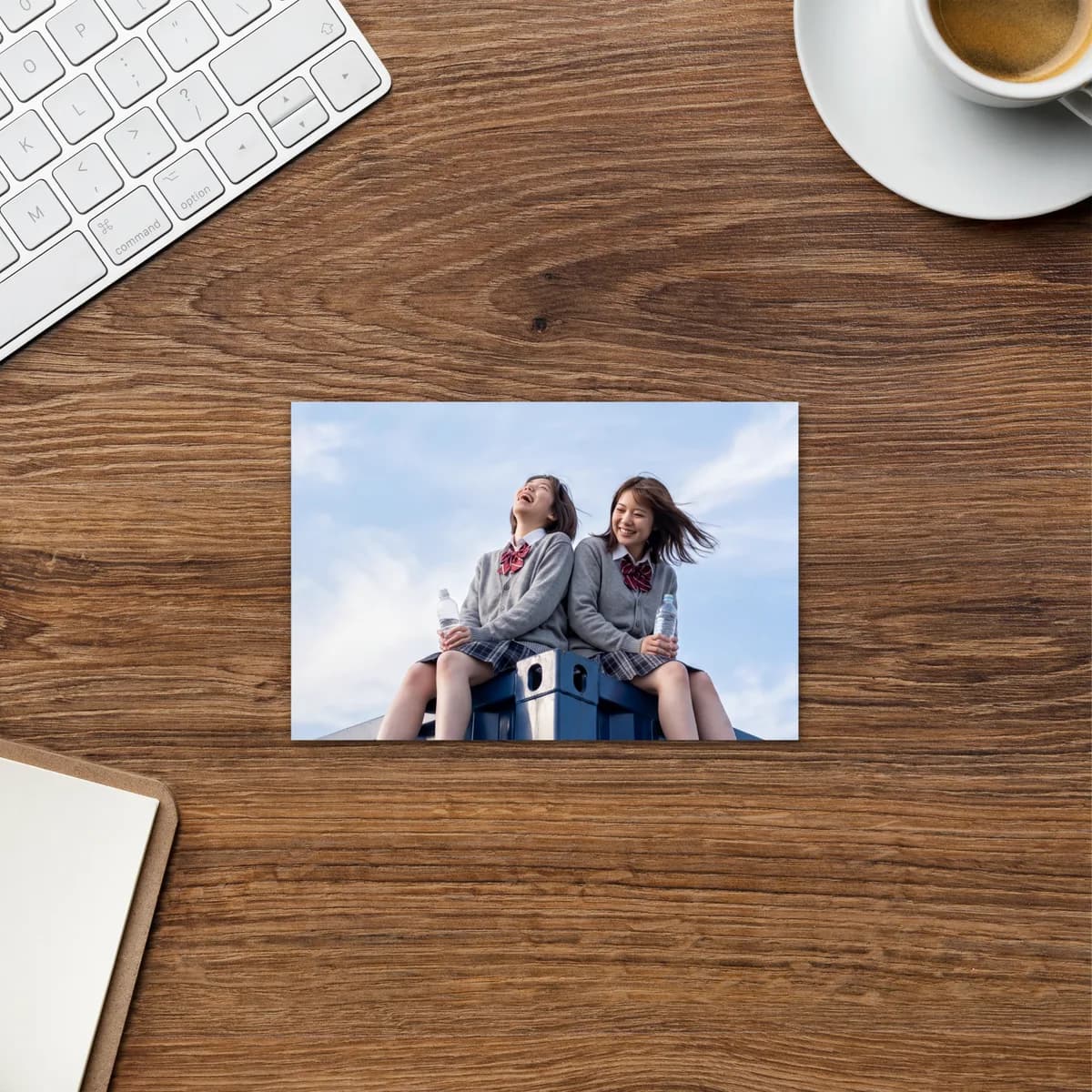 The postcard on a wooden desk between a keyboard and a cup of coffee