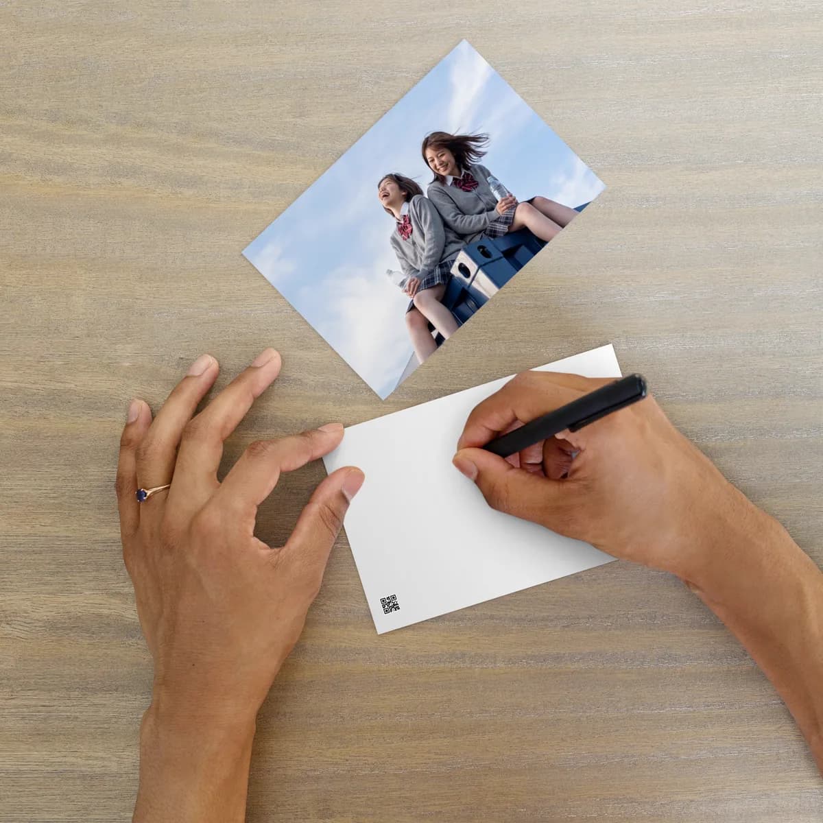 Hands writing a note on the blank back of the postcard, with the printed front lying nearby